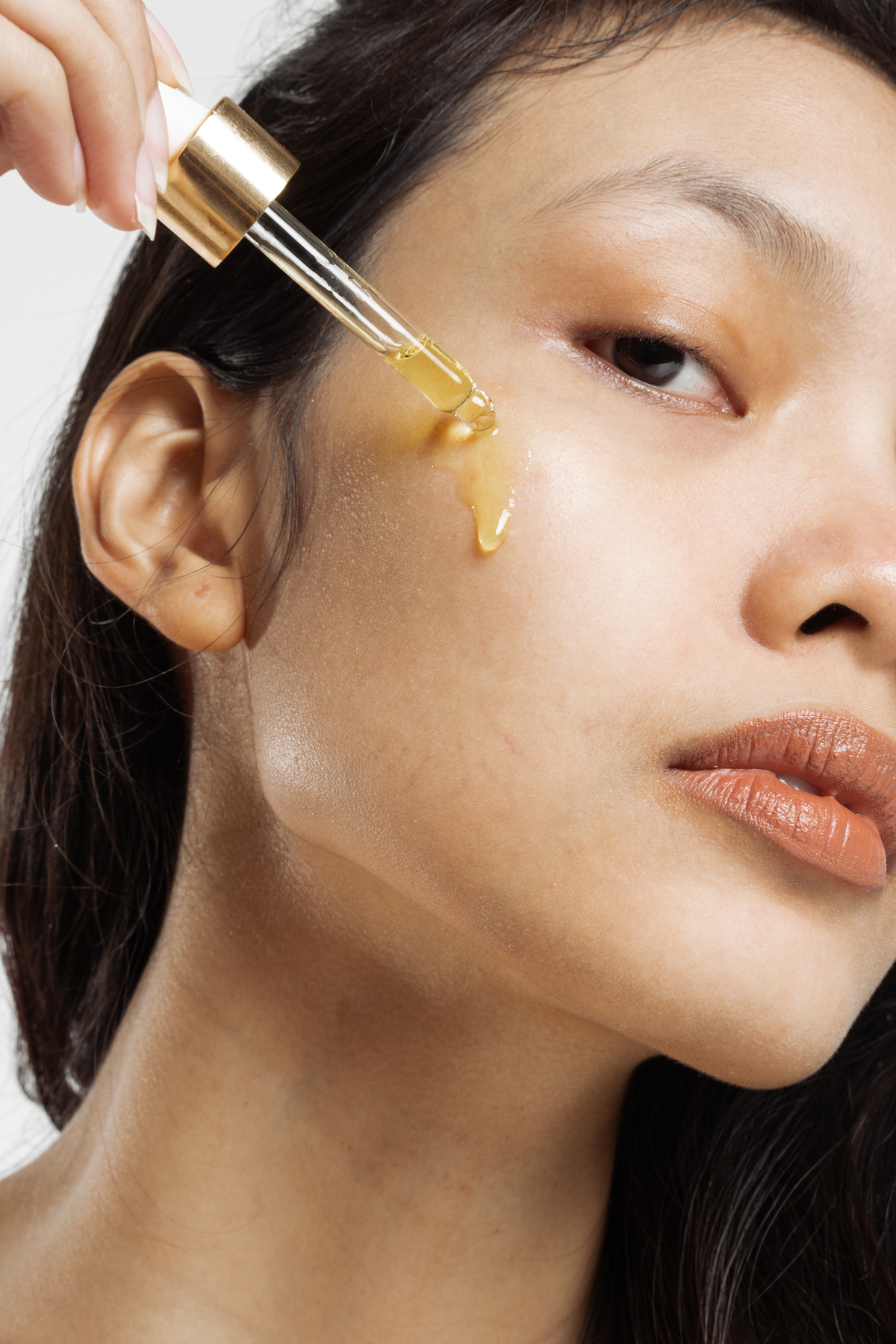 Closeup Portrait of Woman Applying Oil on Face with Dropper