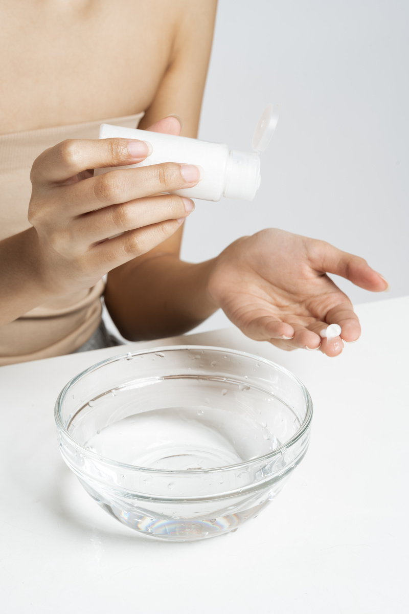 Woman Applying Facial Cream on Hand near Bowl of Water